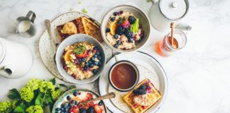 An overhead shot of a waffle, bowls of fruit oatmeal and a cup of coffee. Photo by Brooke Lark on Unsplash