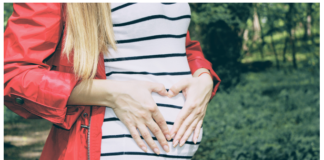 A pregnant woman doing a heart sign in her belly.