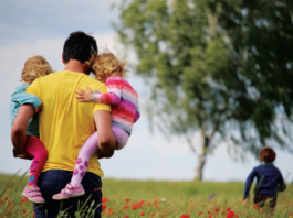 A man holding two kids in a field